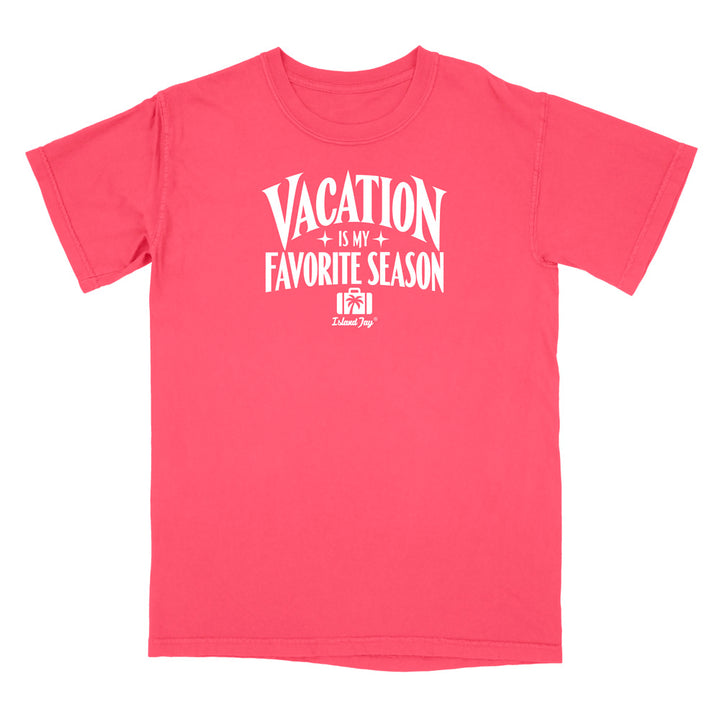 A coral pink short-sleeve t-shirt with a white graphic print on the front that reads 'VACATION IS MY FAVORITE SEASON' with a small camera icon and 'Delilah Dog' logo underneath, shown on a plain white background.