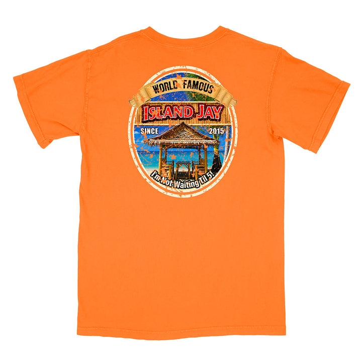 An orange short-sleeve t-shirt with a circular graphic print on the front. The graphic features a tropical beach scene with a thatched-roof gazebo, blue water, and a banner reading 'WORLD FAMOUS ISLAND JAY'.