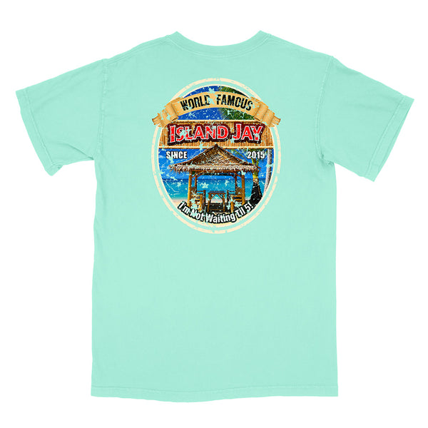A mint green short-sleeve t-shirt with a large circular graphic on the front. The graphic features a tropical beach scene with a thatched-roof gazebo, blue ocean water, and a tan banner reading 'World Famous Island Jay'.