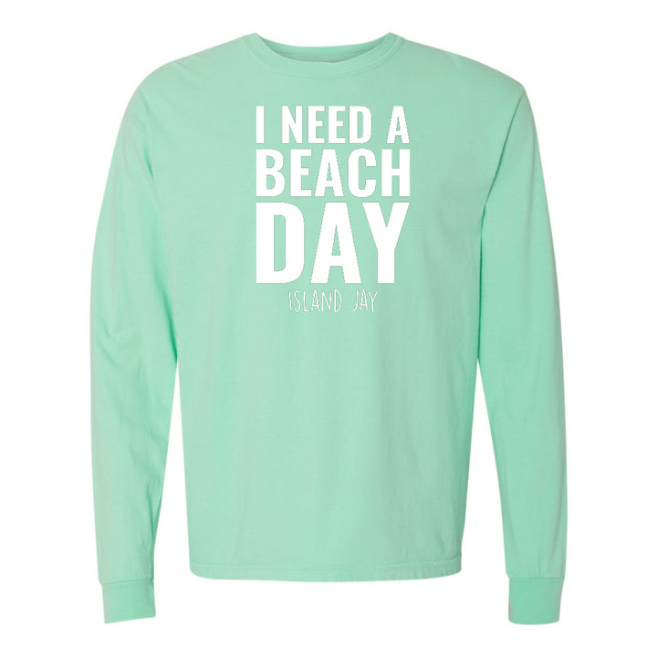 Mint green long-sleeve shirt with 'I NEED A BEACH DAY' text on a white background