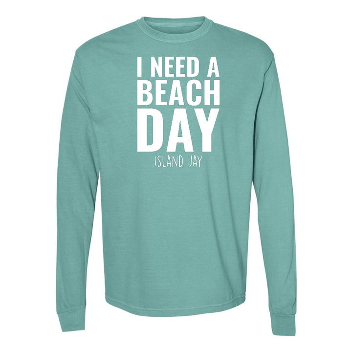 Teal long-sleeve shirt with 'I NEED A BEACH DAY' text on a white background